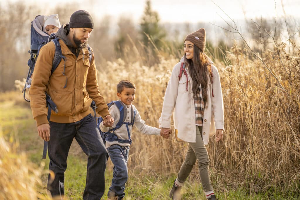 A small young family of four are seen taking a hike on a cool fall day. They are each dressed casually as they explore and enjoy each others company.